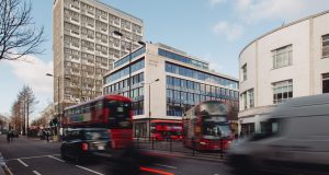Wide shot of United House in Notting Hill with London buses passing by in the foreground